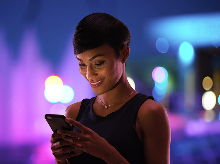 Woman standing looking at her phone with a neon blurred background